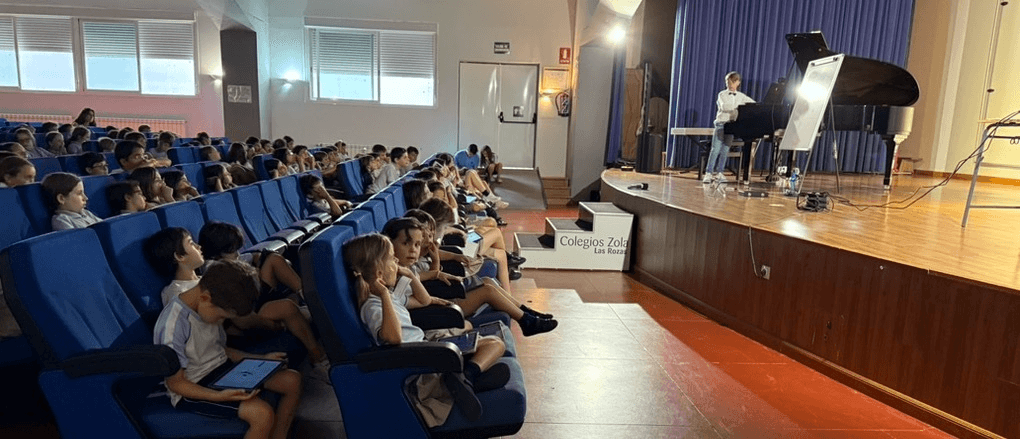 Lucas tocando el piano en una clase-concierto frente a niños en un auditorio escolar